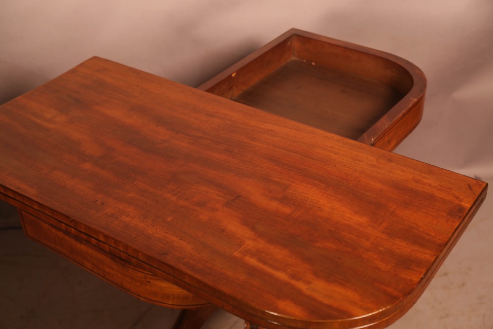 An antique Regency mahogany fold-over games table with a curved frieze, central pedestal support, and splayed legs with brass paw feet. View VII