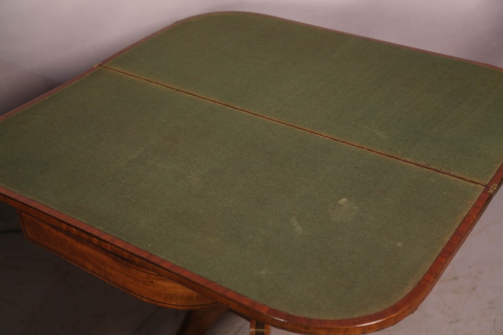 An antique Regency mahogany fold-over games table with a curved frieze, central pedestal support, and splayed legs with brass paw feet. View VIII