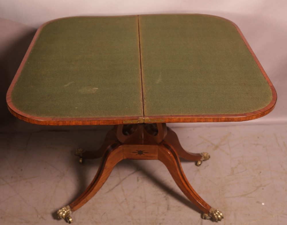 An antique Regency mahogany fold-over games table with a curved frieze, central pedestal support, and splayed legs with brass paw feet. View IX