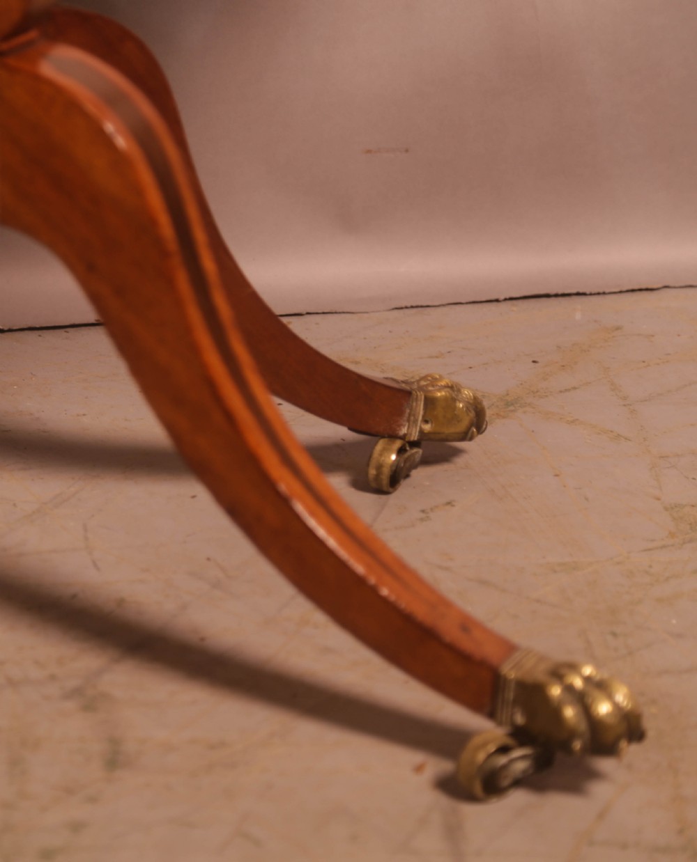 An antique Regency mahogany fold-over games table with a curved frieze, central pedestal support, and splayed legs with brass paw feet. View XI
