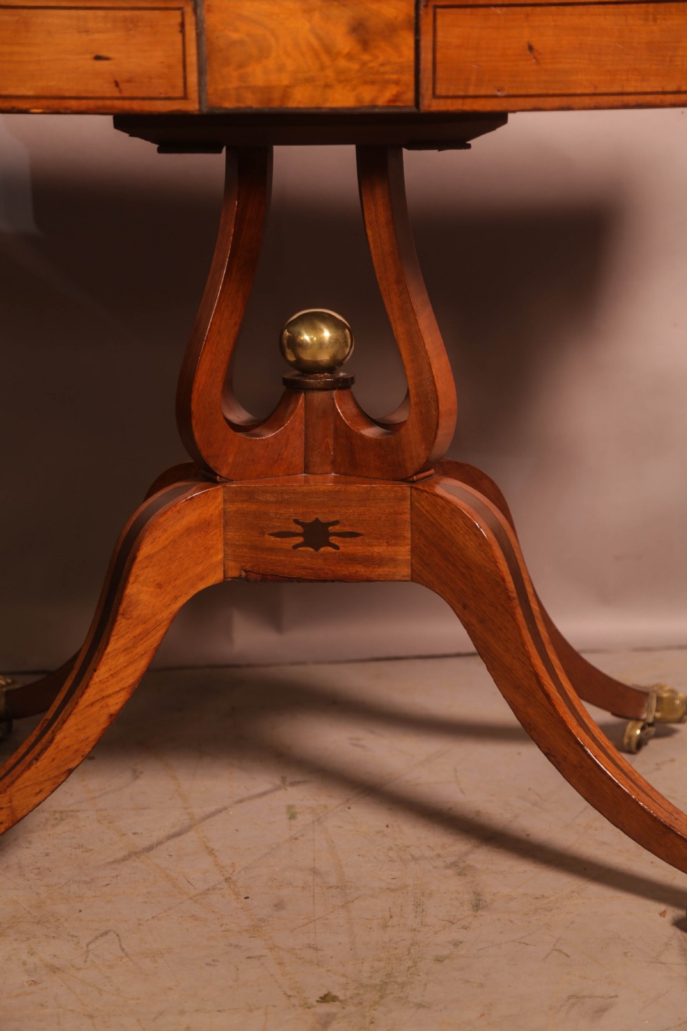 An antique Regency mahogany fold-over games table with a curved frieze, central pedestal support, and splayed legs with brass paw feet. View XII