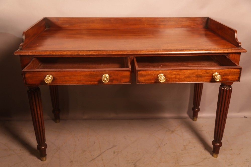 A rectangular mahogany library table featuring a raised back gallery, four drawers with brass ring pulls, and fluted tapering legs. View II