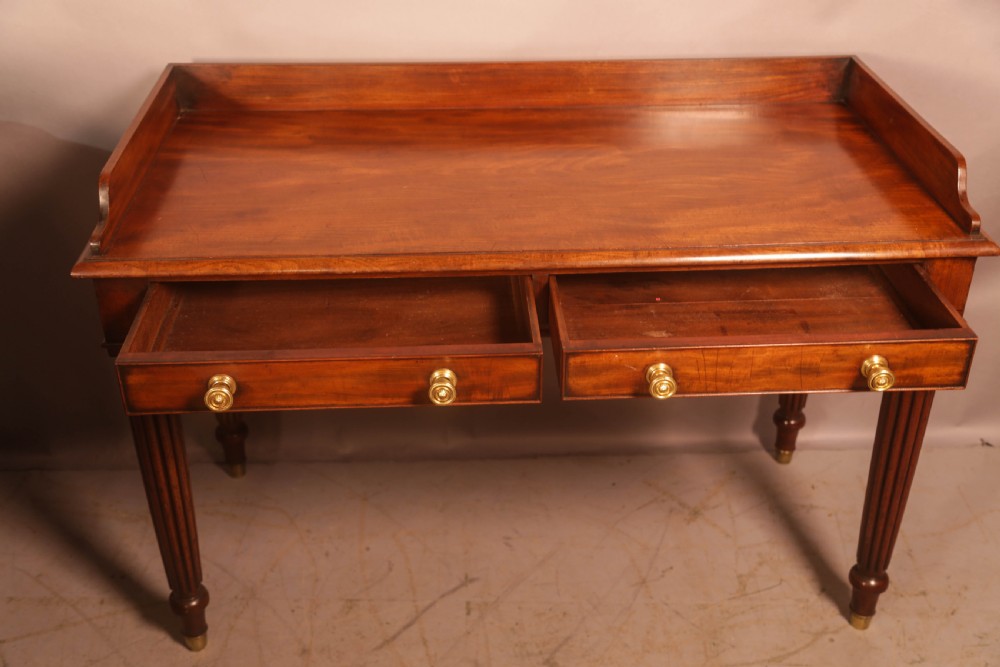 A rectangular mahogany library table featuring a raised back gallery, four drawers with brass ring pulls, and fluted tapering legs. View IV