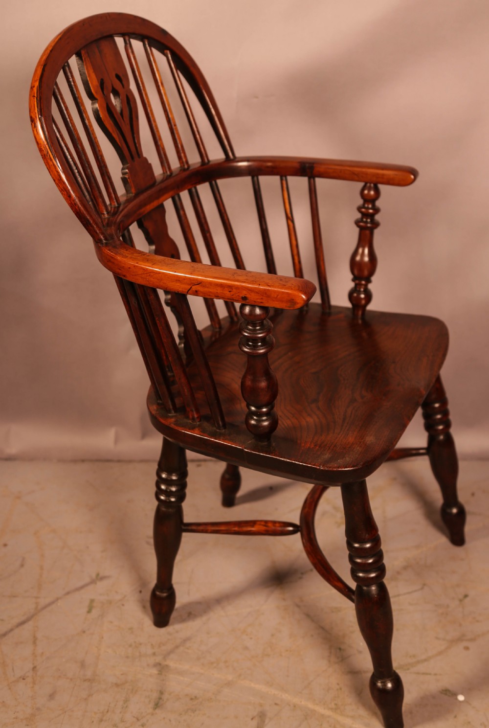 A yew wood Windsor armchair featuring a low back with turned spindles, a pierced fretwork central splat, curved armrests, a shaped solid seat, and turned legs joined by a crinoline stretcher.