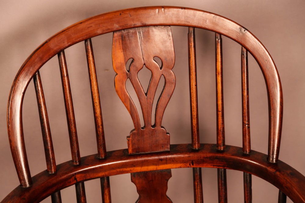 A yew wood Windsor armchair featuring a low back with turned spindles, a pierced fretwork central splat, curved armrests, a shaped solid seat, and turned legs joined by a crinoline stretcher. View X