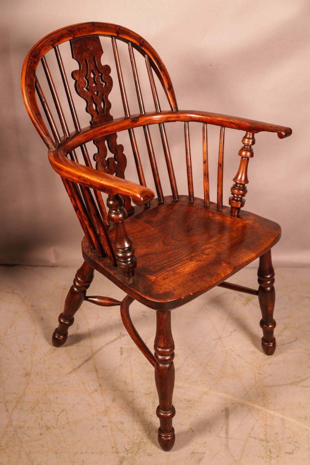 An antique yew wood Windsor armchair featuring a pierced splat, spindle back, shaped wooden seat, and turned legs.