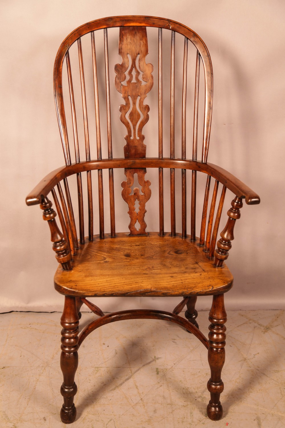 An antique yew wood Windsor armchair featuring a pierced back splat, spindle backrest, turned legs, and a crinoline stretcher.