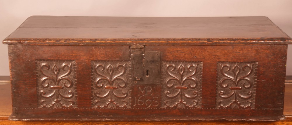 A 17th-century carved dark oak document box with an iron latch, carved initials MB, and date 1695 on the front panel.