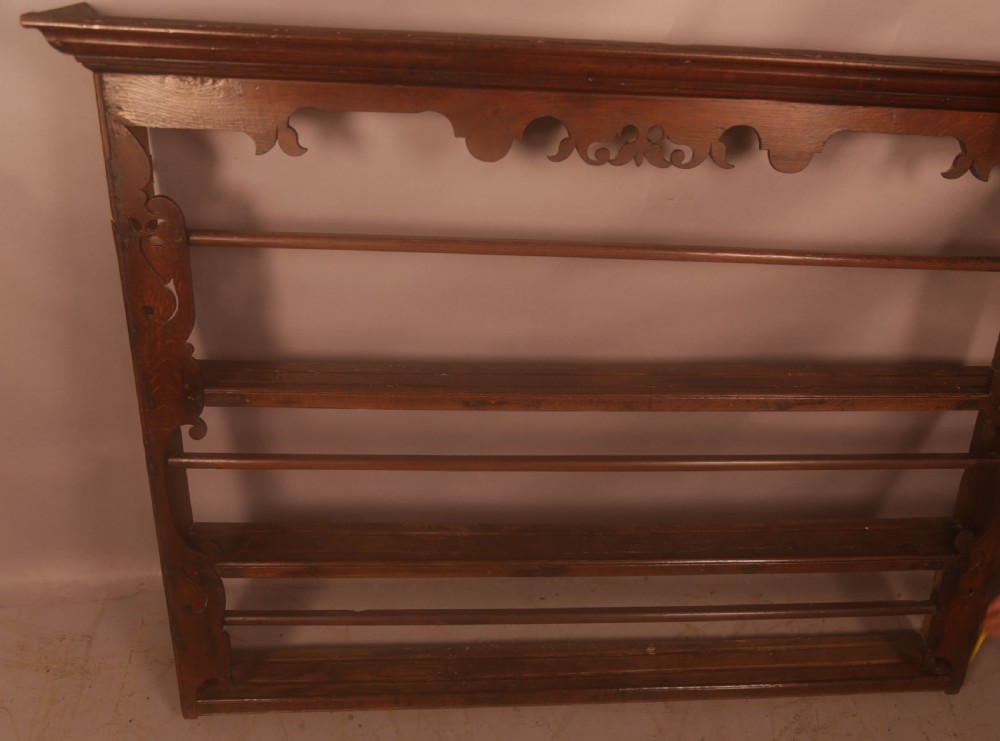 A Georgian dark oak wall-mounted plate rack featuring three horizontal shelves with retaining rails, a moulded top cornice, and decorative fretwork aprons.