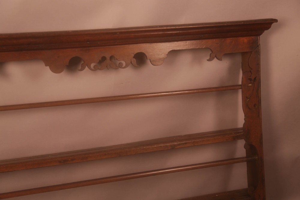 A Georgian dark oak wall-mounted plate rack featuring three horizontal shelves with retaining rails, a moulded top cornice, and decorative fretwork aprons. View IV