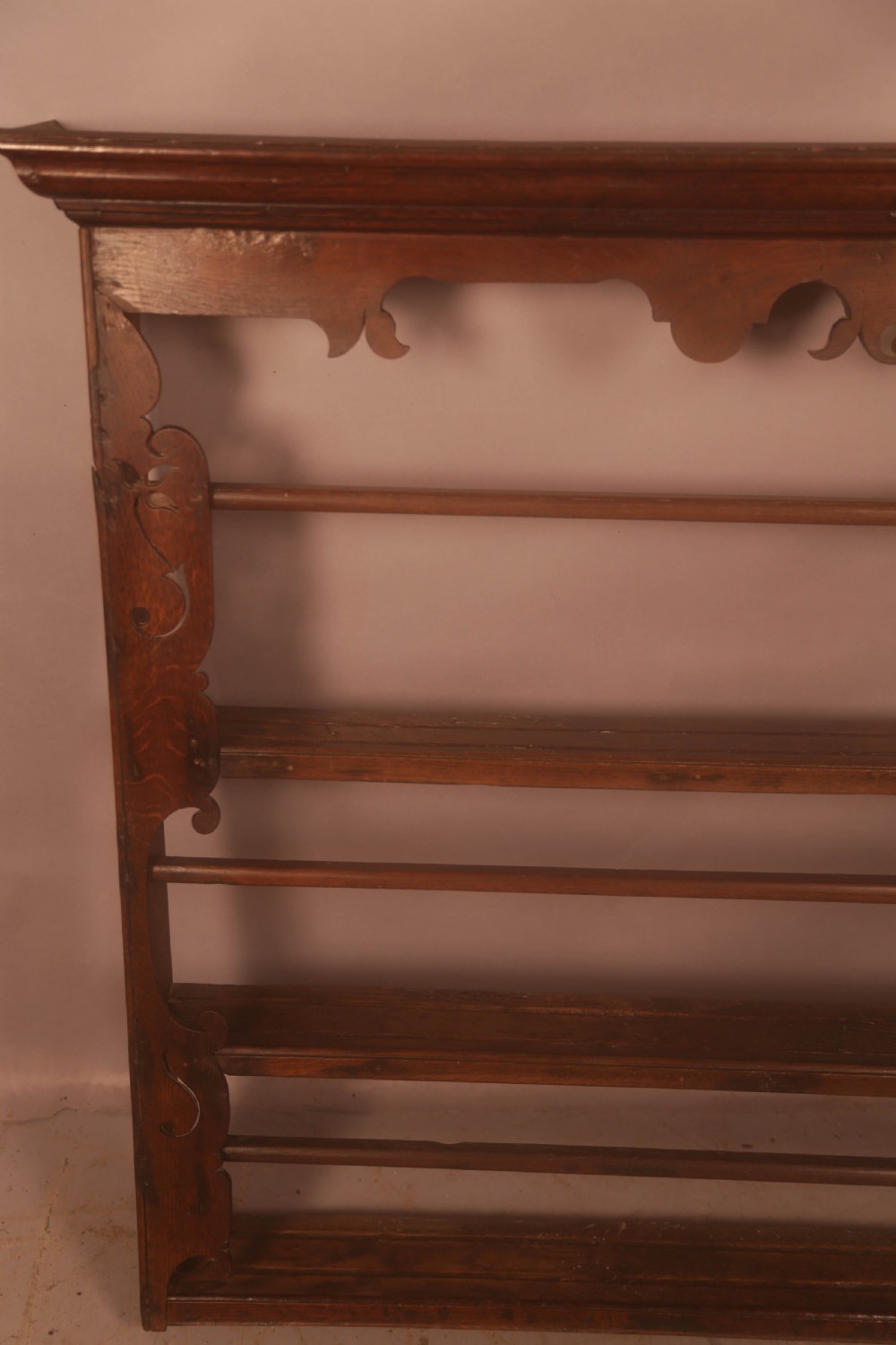 A Georgian dark oak wall-mounted plate rack featuring three horizontal shelves with retaining rails, a moulded top cornice, and decorative fretwork aprons. View VI