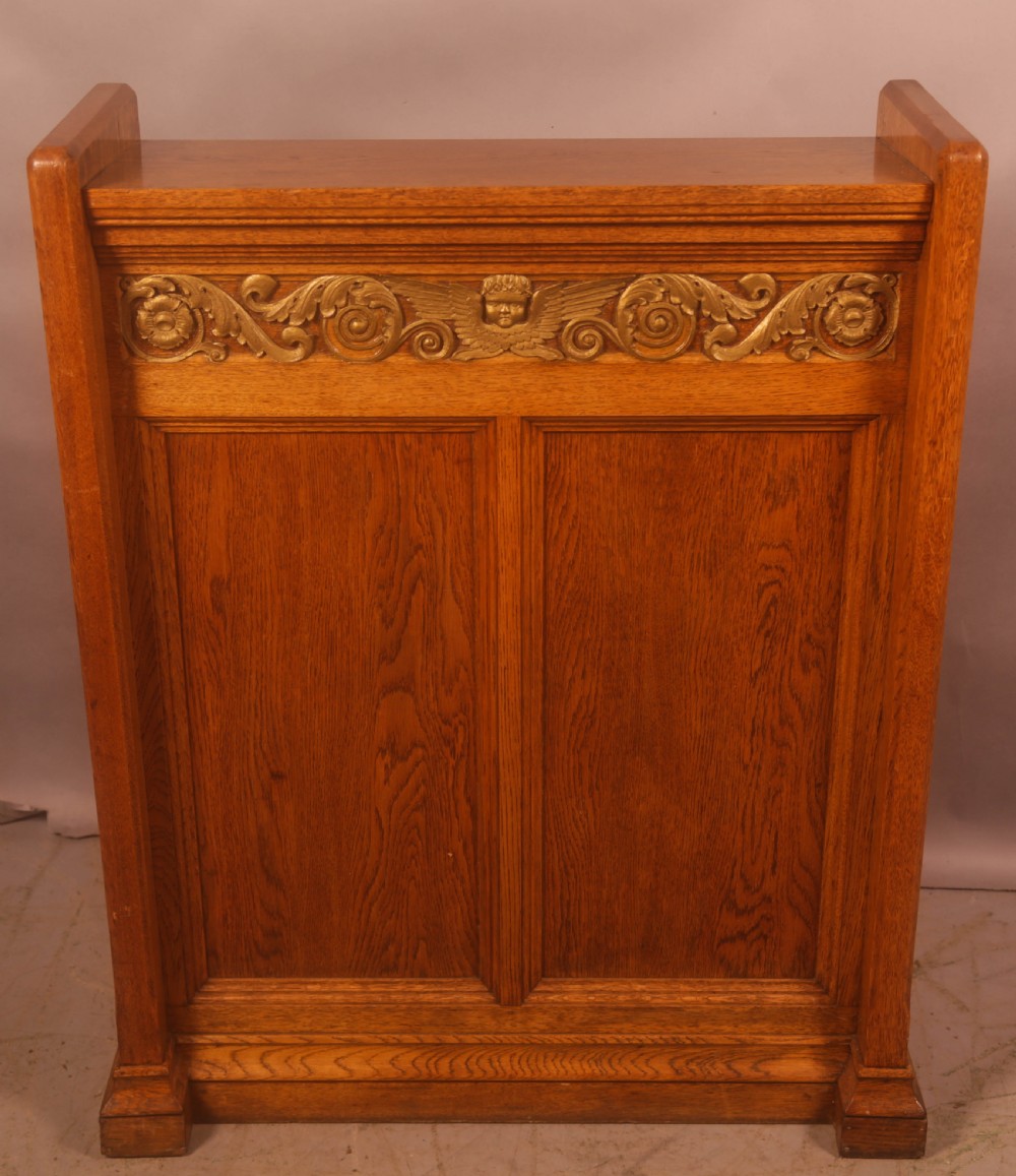 A late Victorian oak reading stand featuring recessed side panels and a decorative cast brass frieze with a central cherub motif.