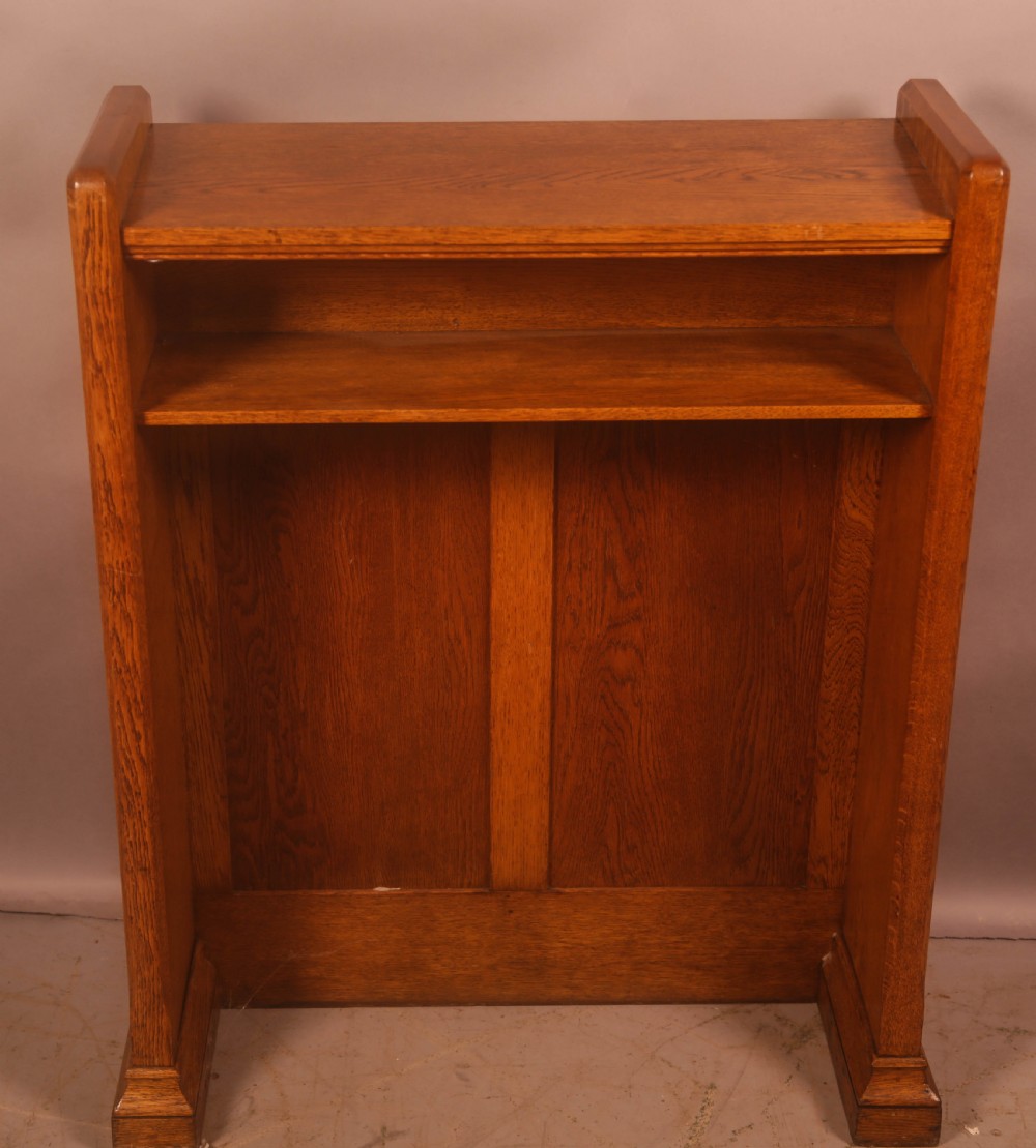 A late Victorian oak reading stand featuring recessed side panels and a decorative cast brass frieze with a central cherub motif. View II