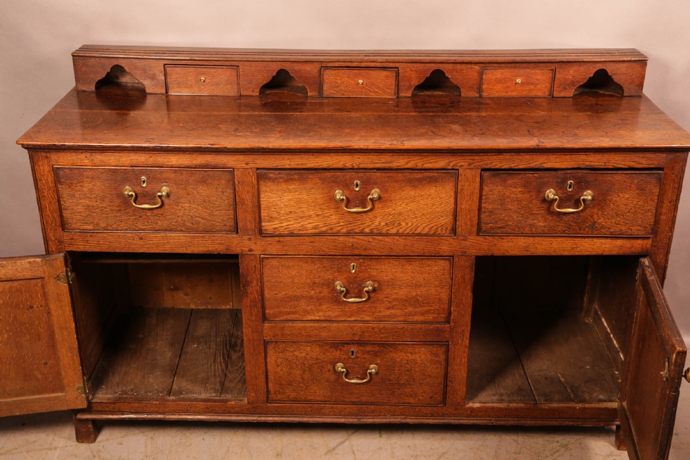 A Georgian oak serving dresser featuring multiple drawers, panelled cupboards, and a raised top tier with small drawers and arched cut-outs. View V