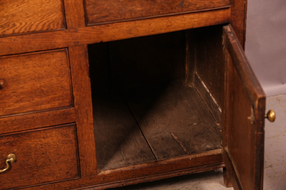 A Georgian oak serving dresser featuring multiple drawers, panelled cupboards, and a raised top tier with small drawers and arched cut-outs. View VII