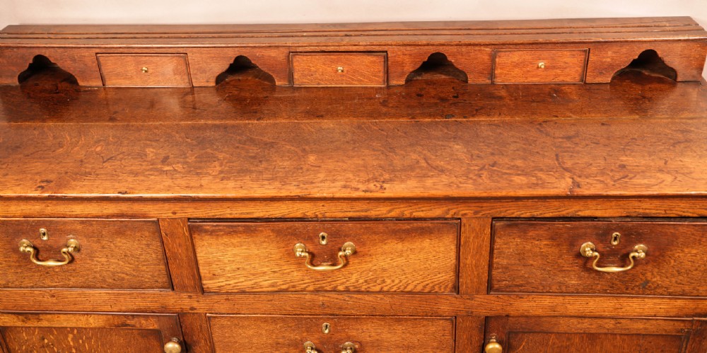 A Georgian oak serving dresser featuring multiple drawers, panelled cupboards, and a raised top tier with small drawers and arched cut-outs. View XII