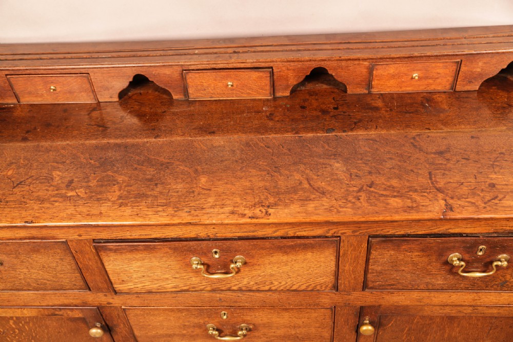 A Georgian oak serving dresser featuring multiple drawers, panelled cupboards, and a raised top tier with small drawers and arched cut-outs. View XIII