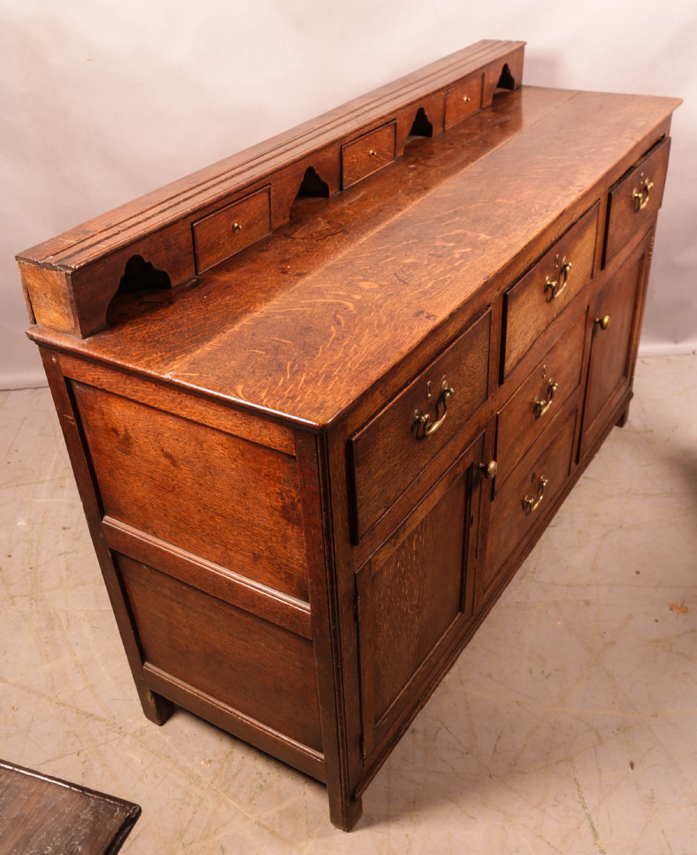 A Georgian oak serving dresser featuring multiple drawers, panelled cupboards, and a raised top tier with small drawers and arched cut-outs. View XVIII
