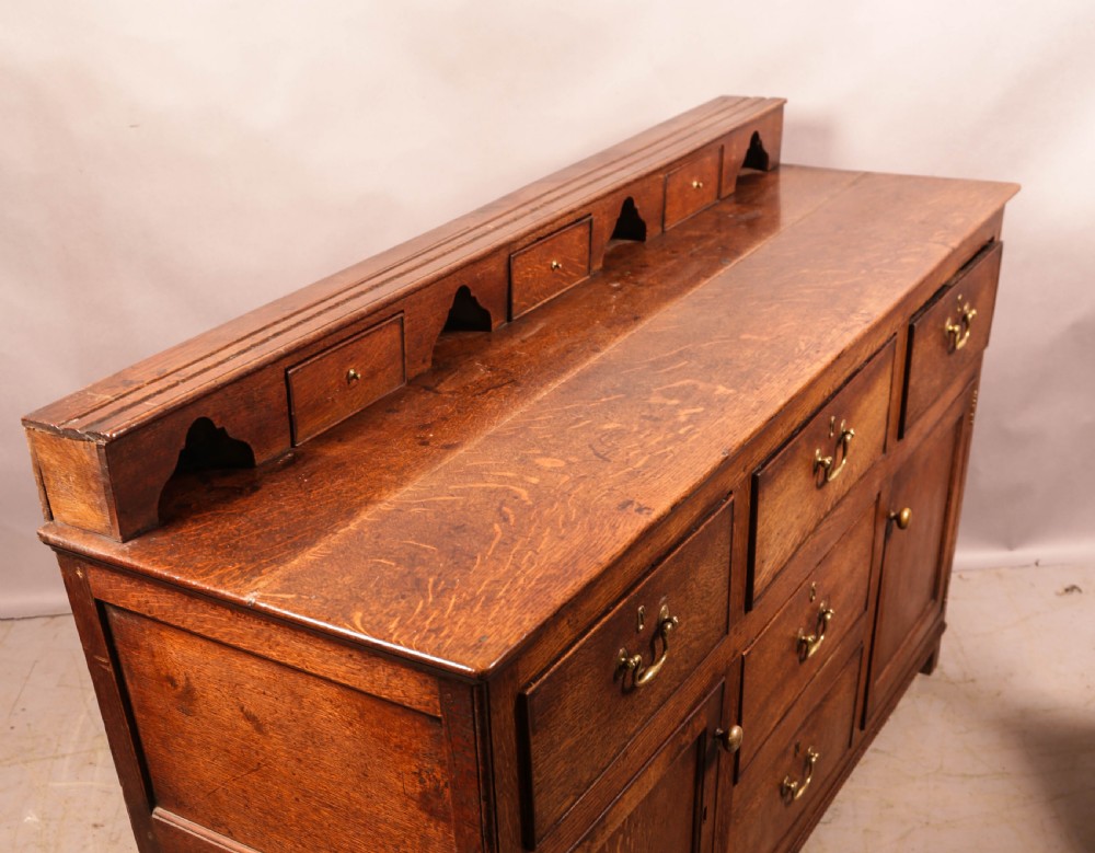A Georgian oak serving dresser featuring multiple drawers, panelled cupboards, and a raised top tier with small drawers and arched cut-outs. View XIX