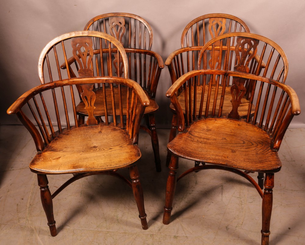 A set of four wooden Windsor armchairs featuring pierced splats, spindle backs, and sculpted seats.