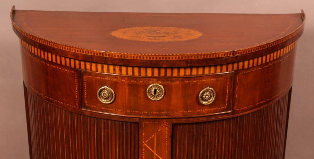 An eighteenth-century mahogany demi-lune cabinet featuring intricate geometric inlay, tambour doors, and brass hardware. View II