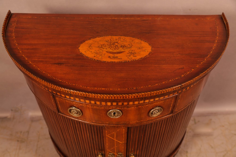 An eighteenth-century mahogany demi-lune cabinet featuring intricate geometric inlay, tambour doors, and brass hardware. View VII