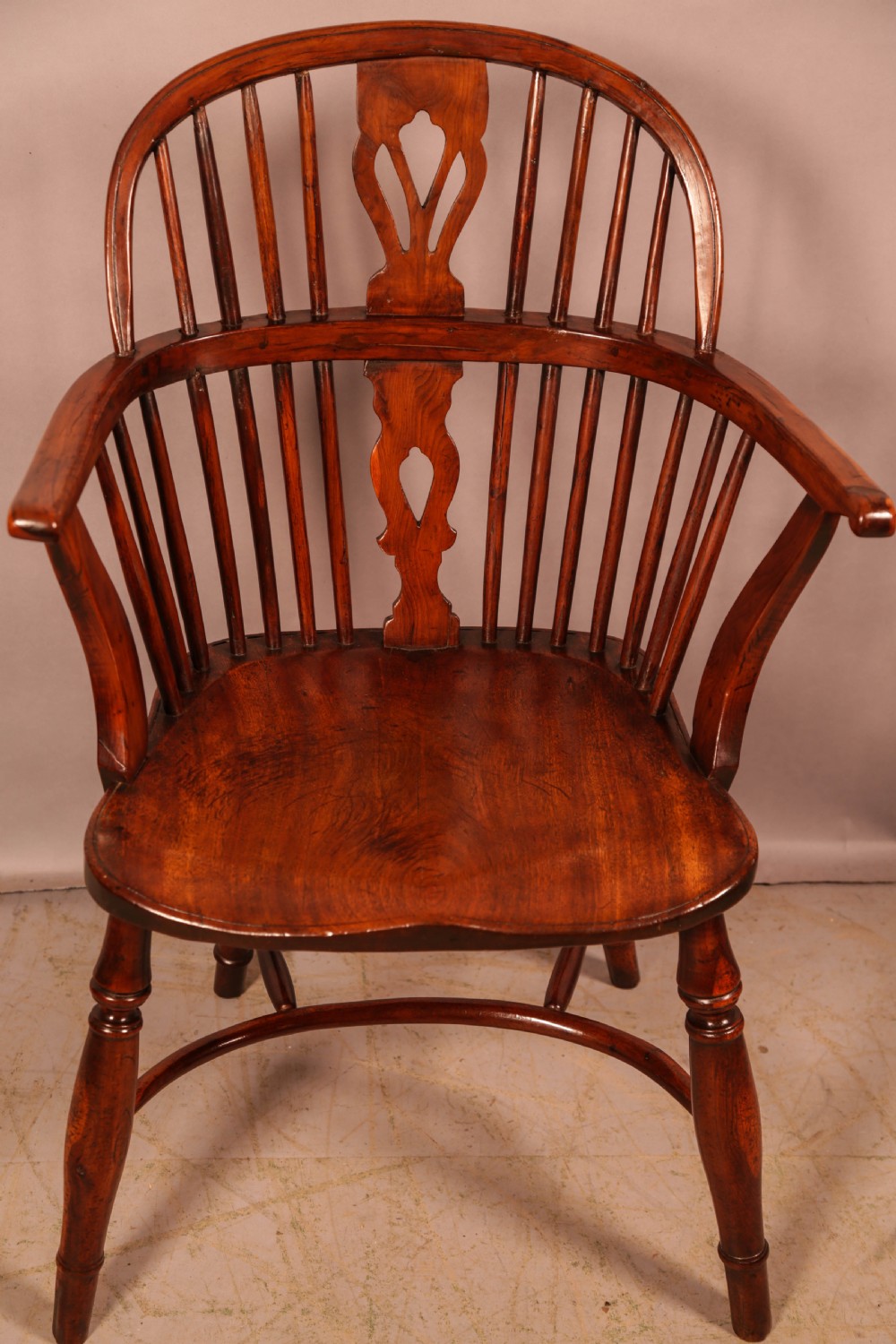 An English yew wood low-back Windsor armchair featuring a pierced splat, spindle back, shaped seat, turned legs, and a curved stretcher.