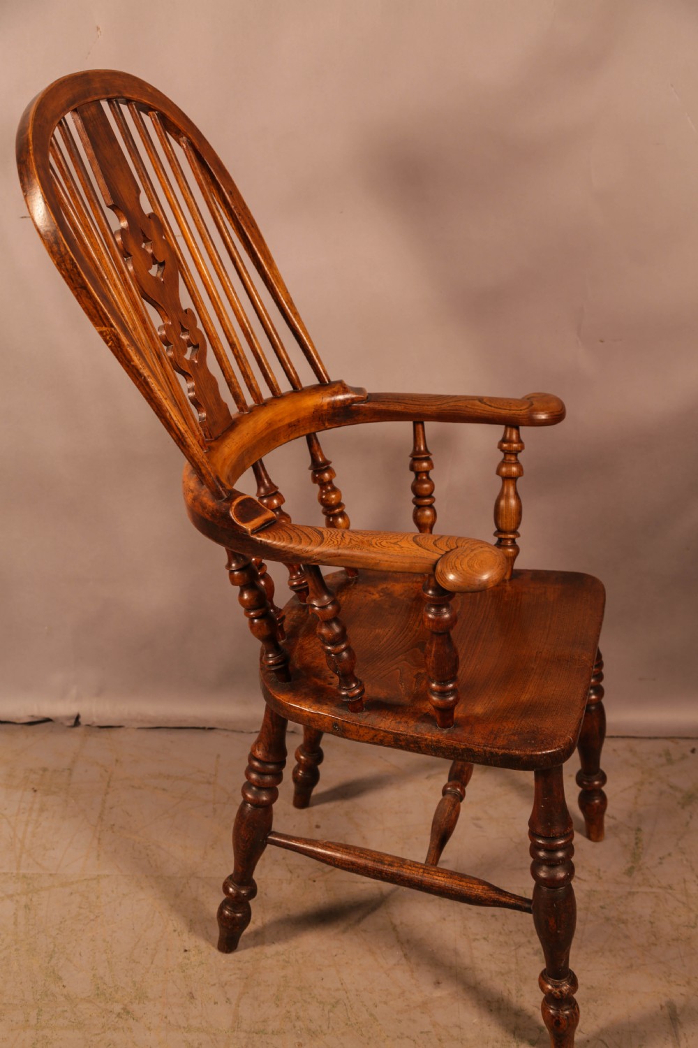 A Victorian broad arm Windsor armchair made from warm brown ash and elm timber, featuring a pierced central splat, turned spindles, a contoured saddle seat, and turned legs with stretchers. View II