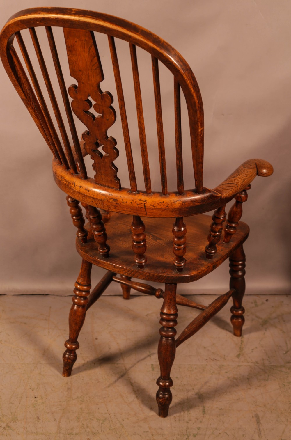 A Victorian broad arm Windsor armchair made from warm brown ash and elm timber, featuring a pierced central splat, turned spindles, a contoured saddle seat, and turned legs with stretchers. View III