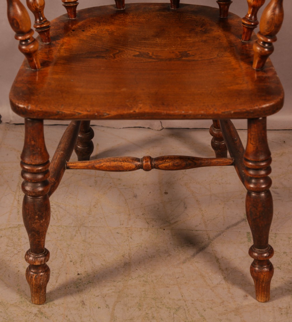 A Victorian broad arm Windsor armchair made from warm brown ash and elm timber, featuring a pierced central splat, turned spindles, a contoured saddle seat, and turned legs with stretchers. View IV