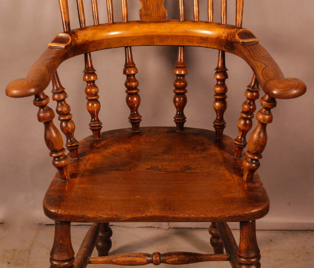 A Victorian broad arm Windsor armchair made from warm brown ash and elm timber, featuring a pierced central splat, turned spindles, a contoured saddle seat, and turned legs with stretchers. View V