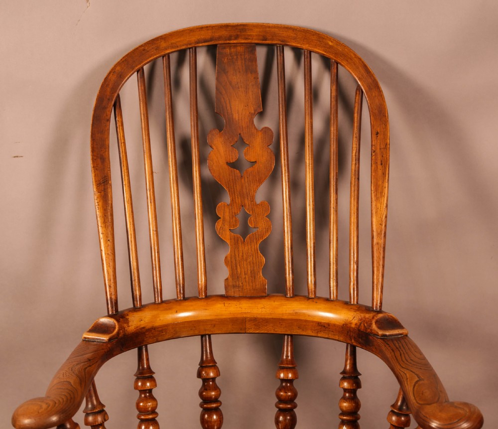 A Victorian broad arm Windsor armchair made from warm brown ash and elm timber, featuring a pierced central splat, turned spindles, a contoured saddle seat, and turned legs with stretchers. View VI