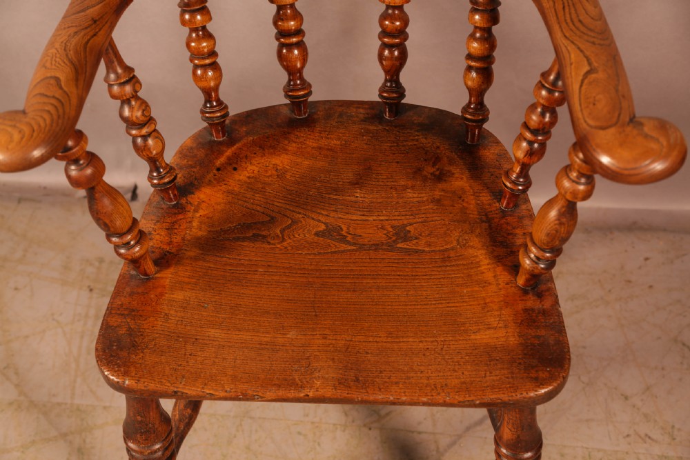 A Victorian broad arm Windsor armchair made from warm brown ash and elm timber, featuring a pierced central splat, turned spindles, a contoured saddle seat, and turned legs with stretchers. View VII