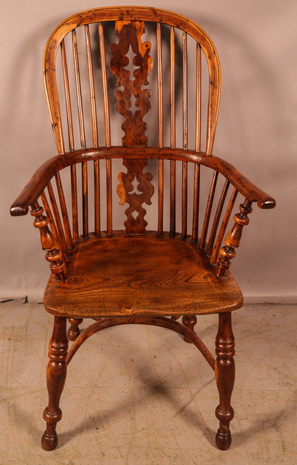 An antique yew wood high-back Windsor armchair featuring a pierced decorative splat, slender spindles, contoured seat, and turned legs with a curved stretcher.