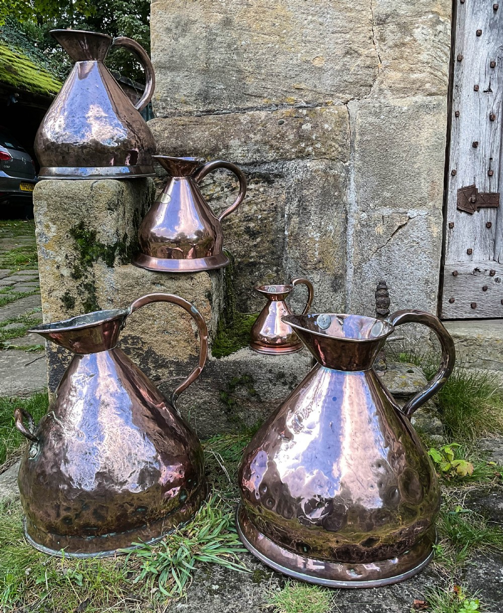 A collection of five graduated nineteenth-century copper harvest jugs featuring hand-beaten surfaces and looped handles.