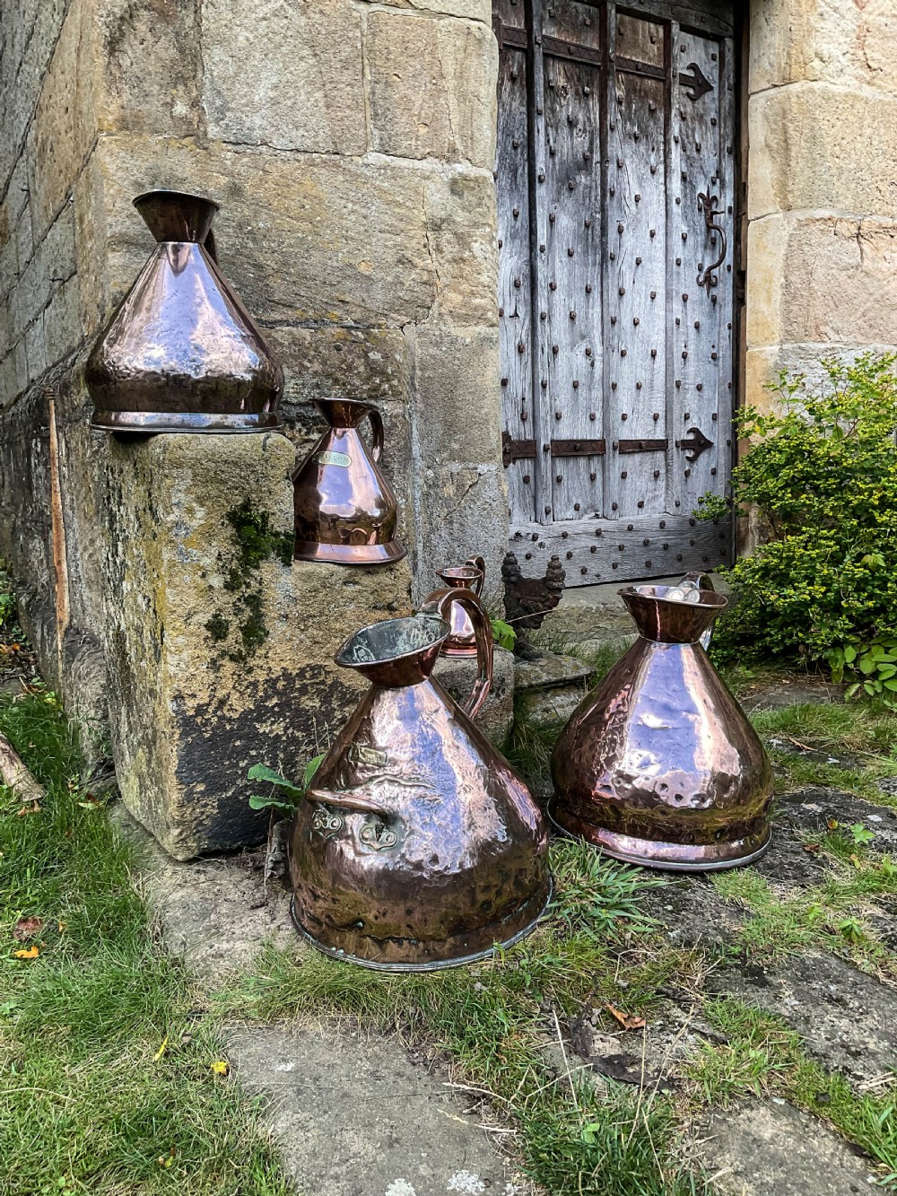 A collection of five graduated nineteenth-century copper harvest jugs featuring hand-beaten surfaces and looped handles. View V