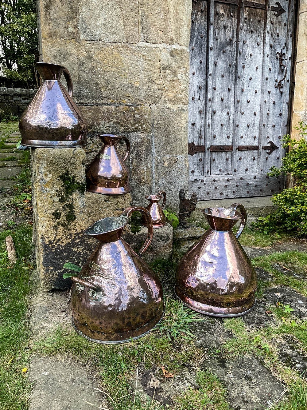A collection of five graduated nineteenth-century copper harvest jugs featuring hand-beaten surfaces and looped handles. View VI