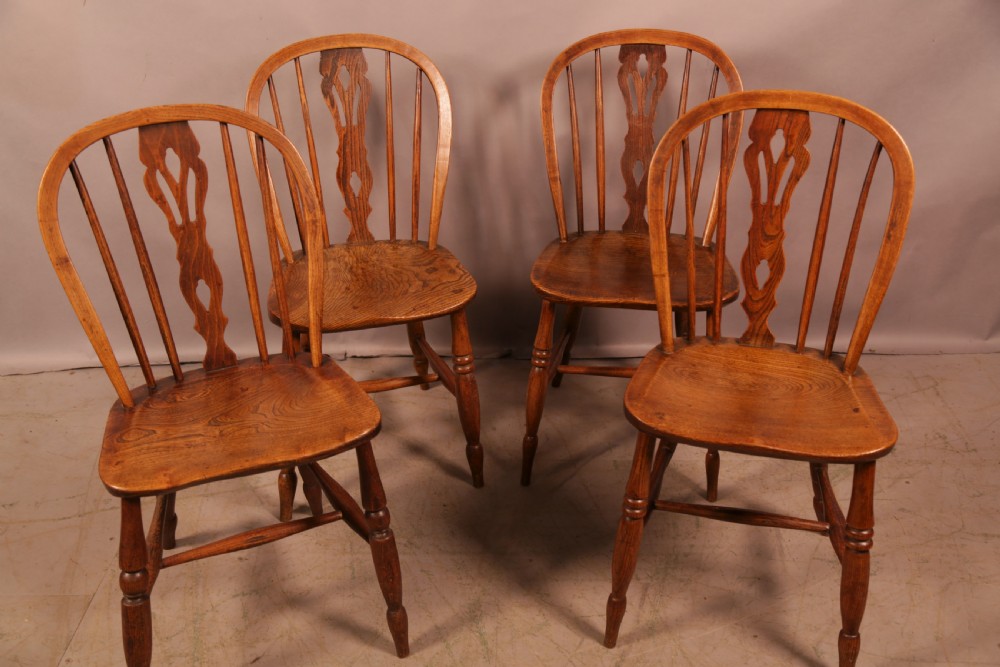 A matching set of four wooden Windsor chairs featuring shaped elm seats, stick-back spindles, and central pierced splats.