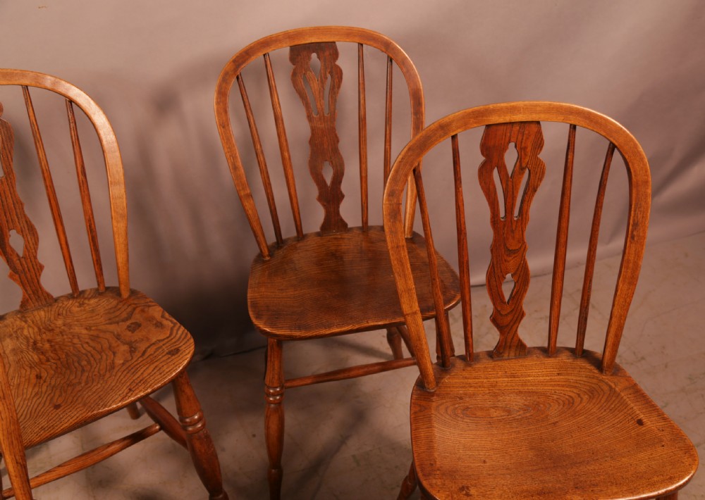 A matching set of four wooden Windsor chairs featuring shaped elm seats, stick-back spindles, and central pierced splats. View III