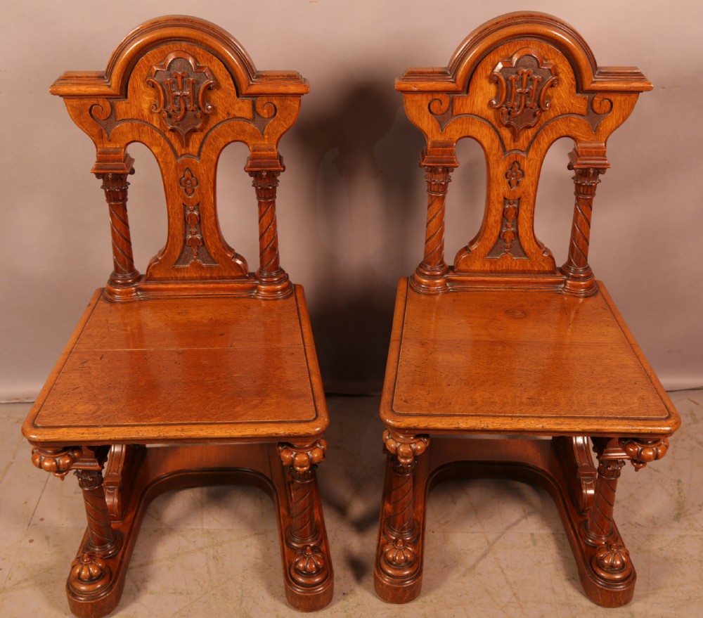 A matching pair of carved oak Victorian hall chairs featuring architectural columns and scrollwork crests.