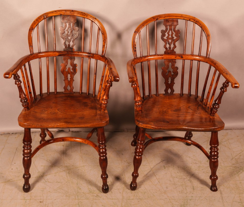 A pair of antique wooden Windsor armchairs featuring pierced splats, spindle backs, and turned legs with rich brown grain.