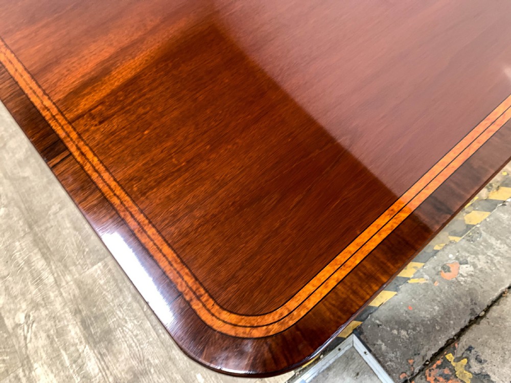An angled view of a polished dark mahogany twin pedestal dining table featuring banded inlay and brass capped feet. View V