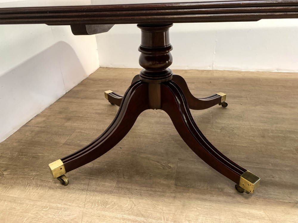 An angled view of a polished dark mahogany twin pedestal dining table featuring banded inlay and brass capped feet. View VII