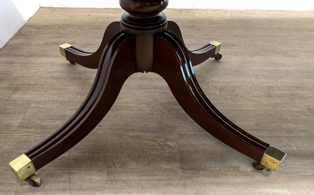 An angled view of a polished dark mahogany twin pedestal dining table featuring banded inlay and brass capped feet. View VIII