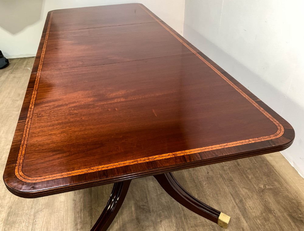 An angled view of a polished dark mahogany twin pedestal dining table featuring banded inlay and brass capped feet. View XII