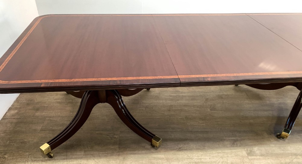 An angled view of a polished dark mahogany twin pedestal dining table featuring banded inlay and brass capped feet. View XIII