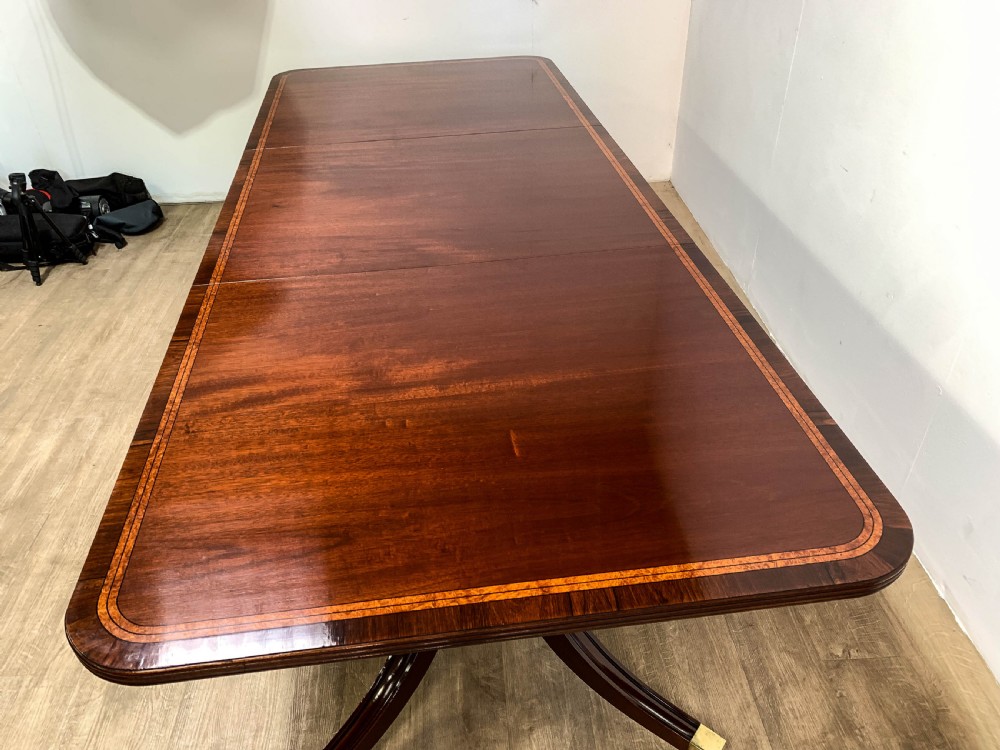 An angled view of a polished dark mahogany twin pedestal dining table featuring banded inlay and brass capped feet. View XIV