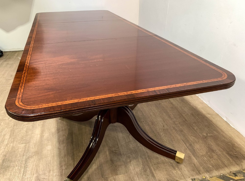 An angled view of a polished dark mahogany twin pedestal dining table featuring banded inlay and brass capped feet. View XVII