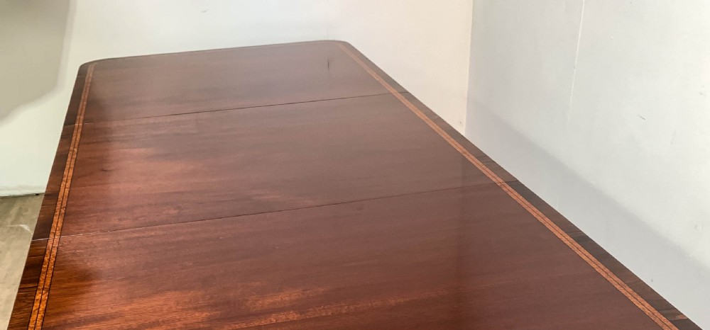 An angled view of a polished dark mahogany twin pedestal dining table featuring banded inlay and brass capped feet. View XVIII