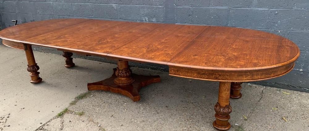 An extended Victorian pollard oak dining table featuring carved columnar legs, a central pedestal base, and a figured wood grain top.